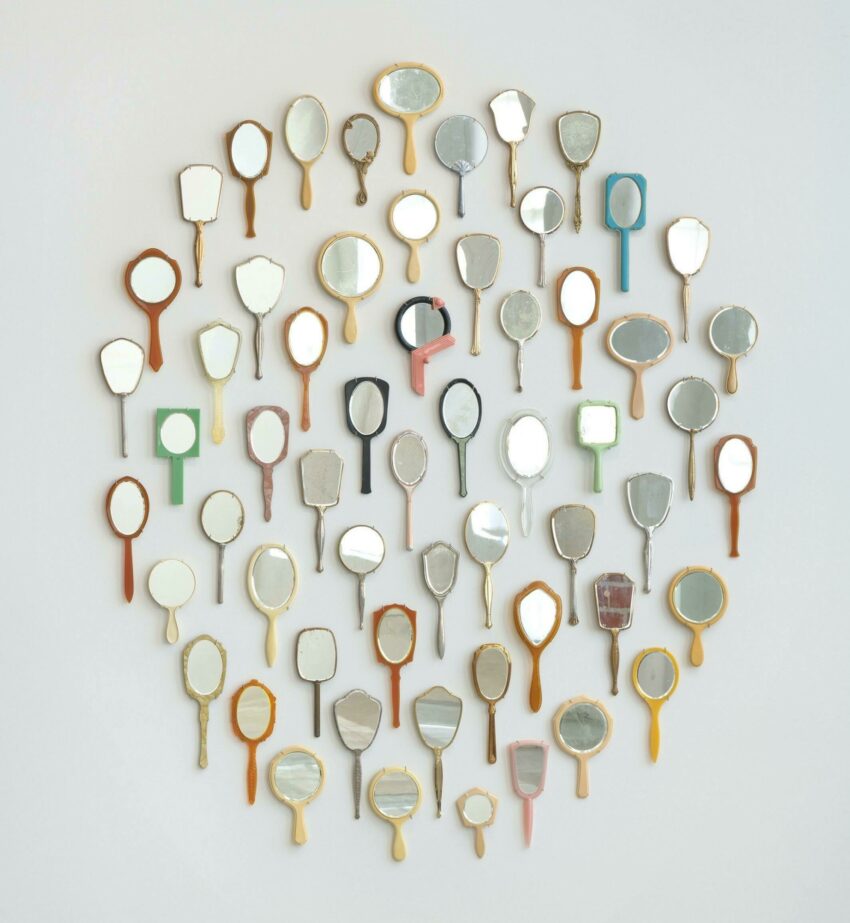 Installation of found hand mirrors arranged in an oval on a wall.