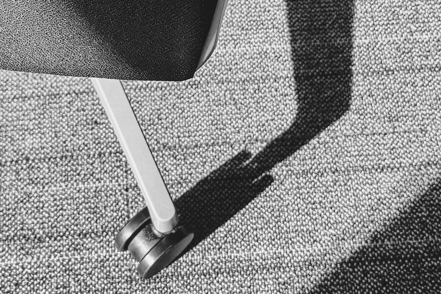 Black-and-white photo of the underside of an office chair on castors, shadow falling across carpet.