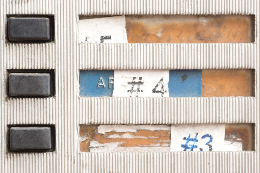 Weathered apartment intercom panel; the paper name strips are torn, taped over and mostly illegible.